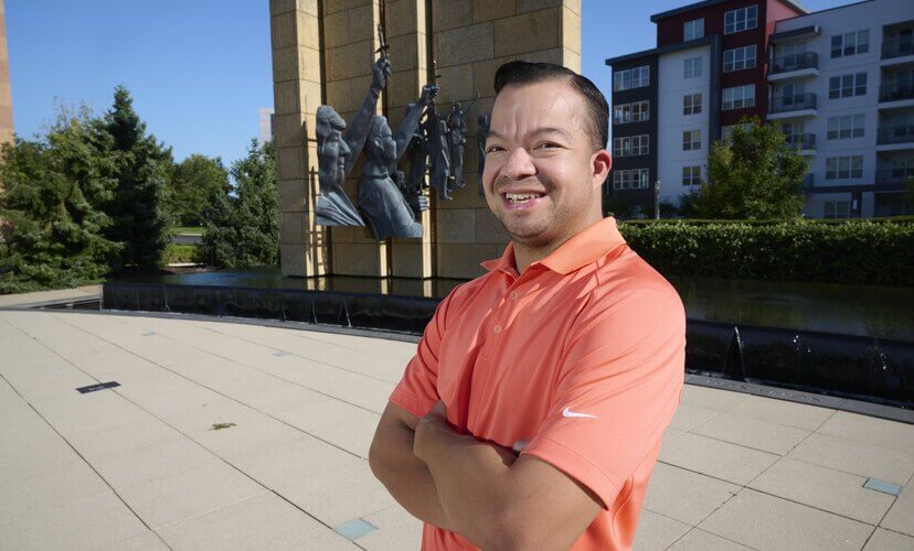 Joe, a Mid-America Transplant employee, stands in front of the donor memorial sculpture fountain, and is wearing an orange-pink Nike polo