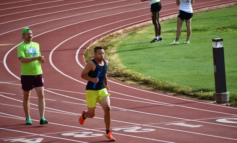 Joe, wearing neon yellow shorts and a navy tank top, running a relay race at the 2022 Transplant Games of America. His teammate behind him is wearing an MT United shirt.