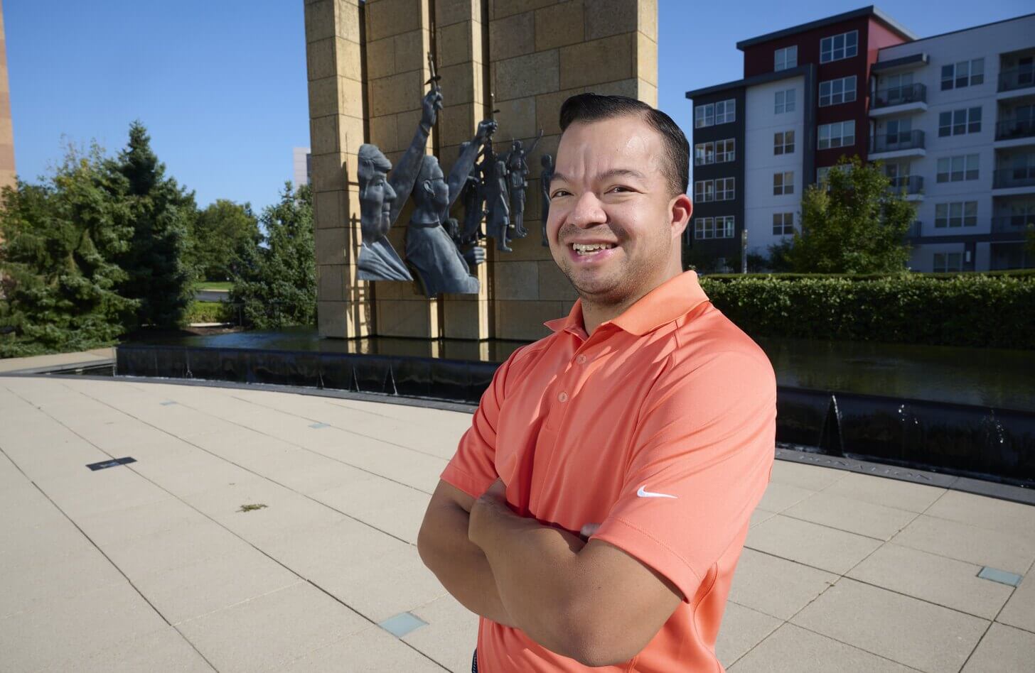 Joe, a Mid-America Transplant employee, stands in front of the donor memorial sculpture fountain, and is wearing an orange-pink Nike polo